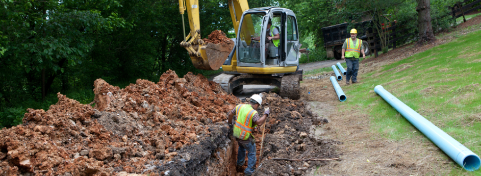 Workers with backhoe installing pipeline.